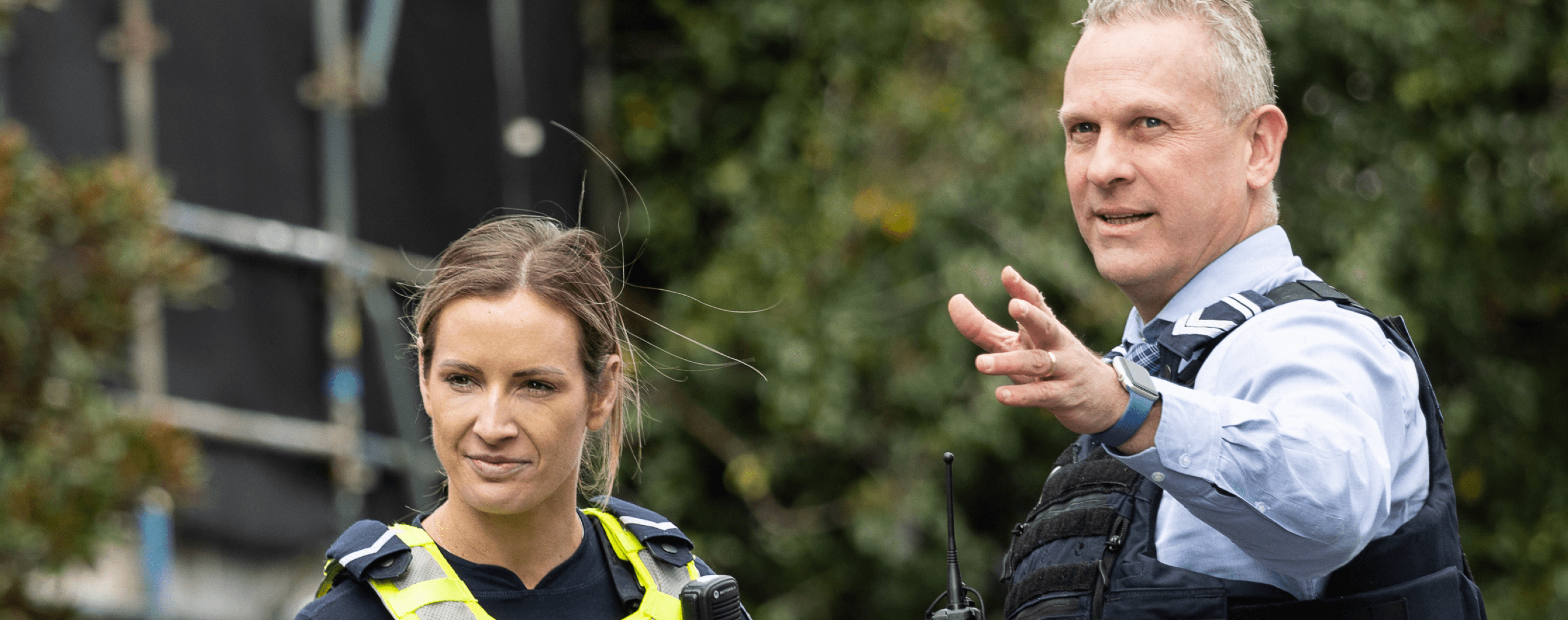 Male Police officer gesturing into the distance off camera while a female officer looks to where he is pointing